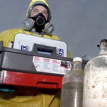 An image of a man dressed in full lab gear carrying meth lab contaminants.